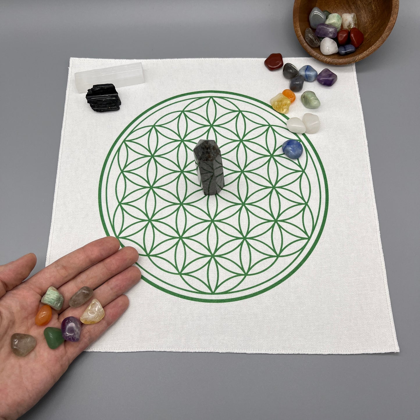 12 Inch Flower of Life Crystal Grid Cloth with Tumbled Crystals and a Crystal Tower on it Showing a Hand Placing Tumbled Crystals