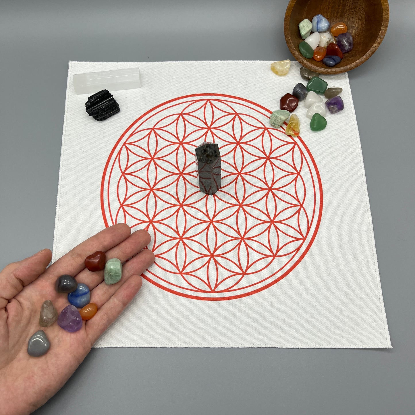 12 Inch Flower of Life Crystal Grid Cloth with Tumbled Crystals and a Crystal Tower on it Showing a Hand Placing Tumbled Crystals