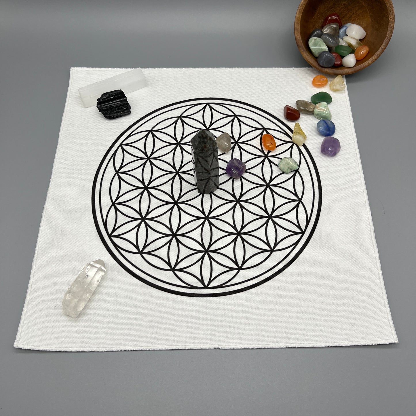 12 Inch Flower of Life Crystal Grid Cloth with Tumbled Crystals and a Crystal Tower Placed on it and complete with Clear Quartz Point, Selenite Wand, and Black Tourmaline Displaying the Grid Cloth in Use.