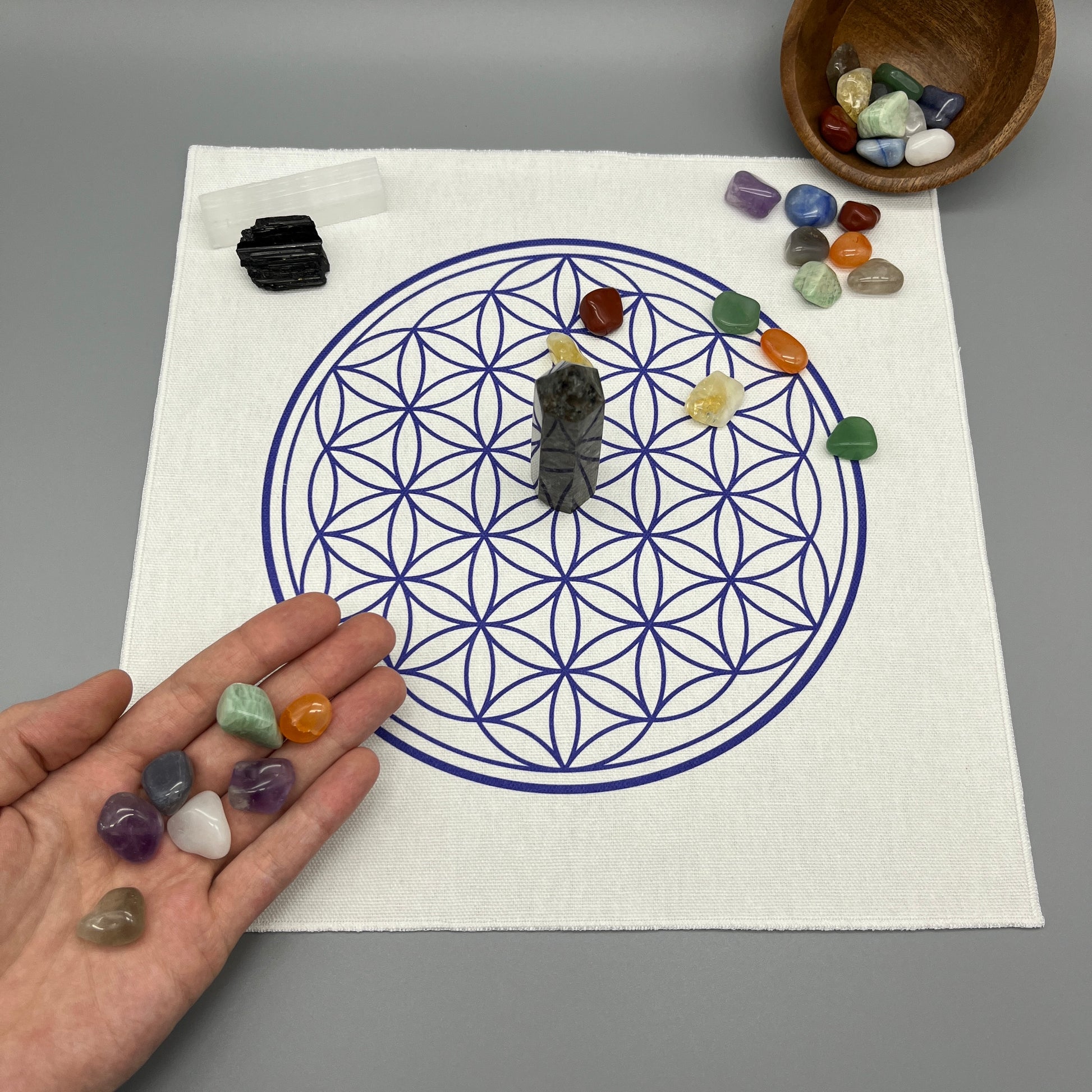 12 Inch Flower of Life Crystal Grid Cloth with Tumbled Crystals and a Crystal Tower on it Showing a Hand Placing Tumbled Crystals