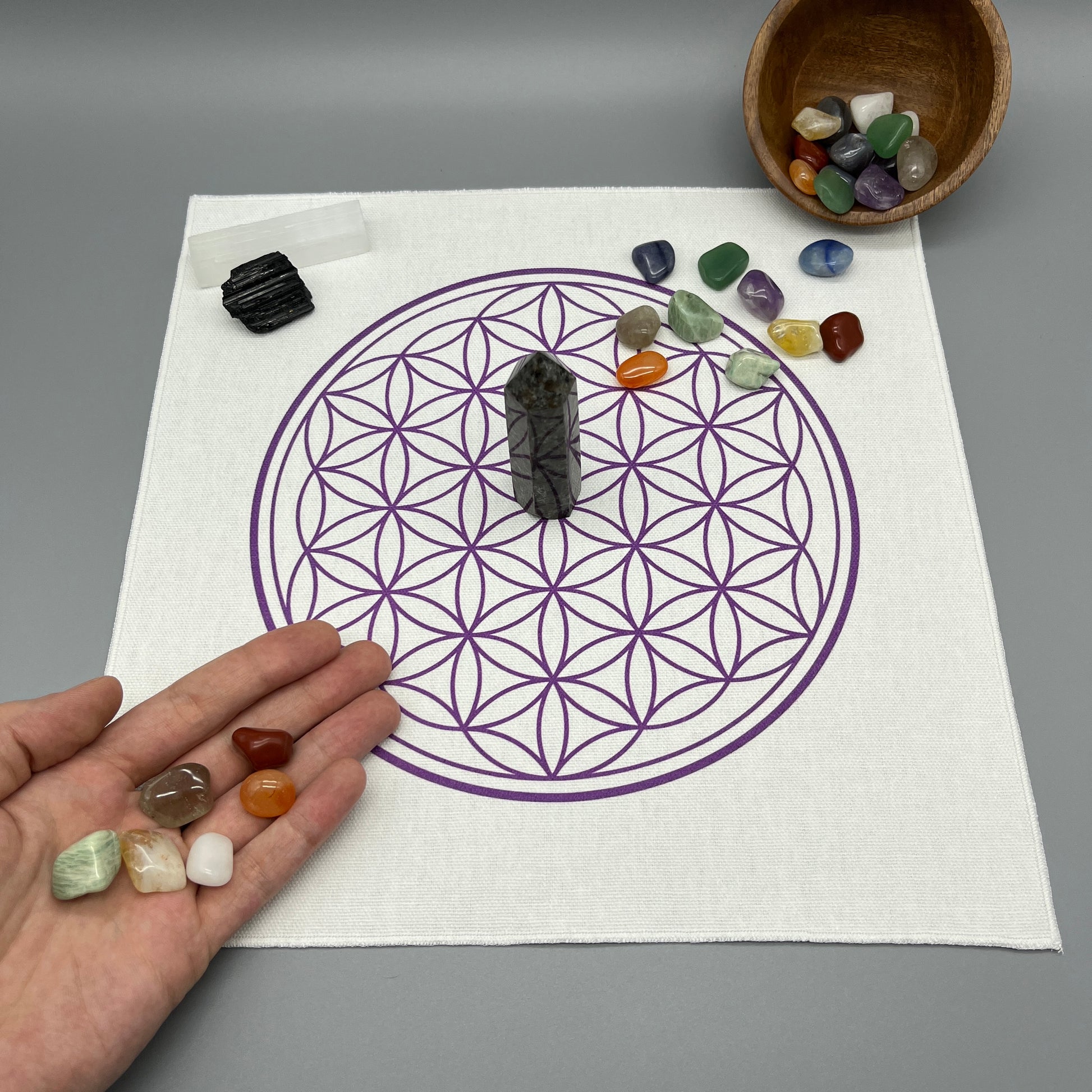 12 Inch Flower of Life Crystal Grid Cloth with Tumbled Crystals and a Crystal Tower on it Showing a Hand Placing Tumbled Crystals