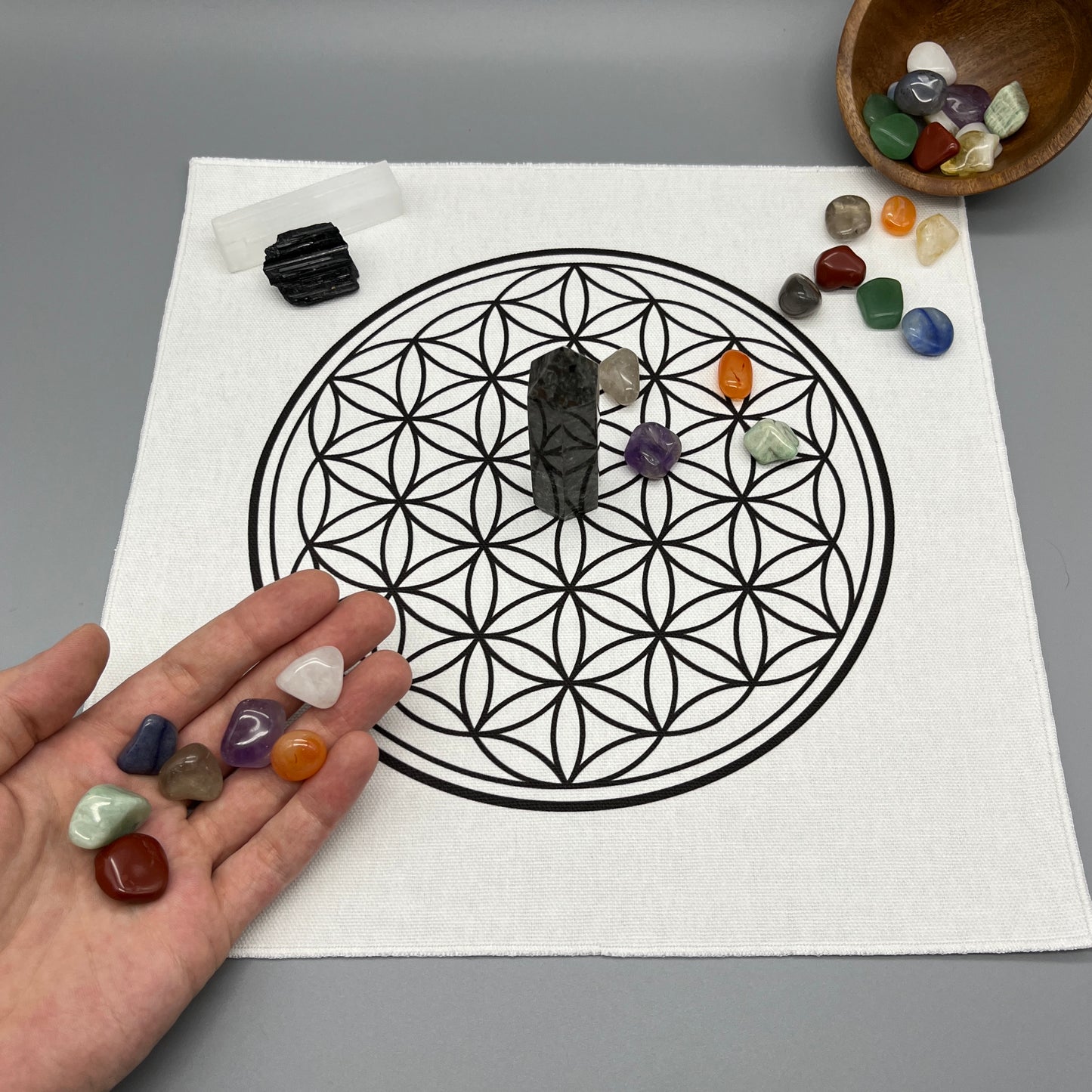 12 Inch Flower of Life Crystal Grid Cloth with Tumbled Crystals and a Crystal Tower on it Showing a Hand Placing Tumbled Crystals